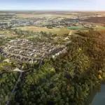 Aerial view of the Empire Riverland community master plan, showcasing rows of modern homes nestled between a winding river with kayakers and a dense, green forest at sunset.