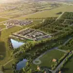 Aerial view of The Heights of Harmony East residential development showing planned rows of modern homes, integrated green spaces, two ponds, and surrounding lush forests under a golden sunset.