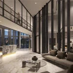 Luxury lobby interior at The Wilmot Condos featuring a marble concierge desk, high ceilings with floor-to-ceiling glass partitions, a modern fireplace lounge, and polished stone flooring.