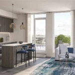 Modern open-concept kitchen and living area at The Wilmot, showcasing wood-grain cabinetry, a large island with blue velvet stools, and bright floor-to-ceiling windows leading to a private balcony.