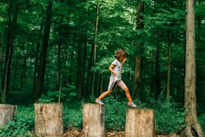 Young Girl Walking Across Tree Stumps. - Stocksy txpe2ea0be2km7300 OriginalDelivery 3327451 300x200