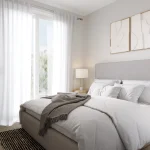 Bright modern bedroom rendering with a upholstered king bed, white sheer curtains leading to a balcony, and neutral decor at Marquis Modern Towns