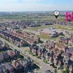 Aerial drone view of the New Kleinburg master-planned suburban housing development, showcasing rows of modern homes, a community school, local green spaces, and map markers indicating proximity to the Highway 427 off-ramp and on-ramp.