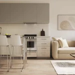 Interior view of a contemporary studio suite at The Rebecca Condos featuring an open-concept kitchen with stainless steel appliances, light wood flooring, and a sunlit living area with minimalist decor.