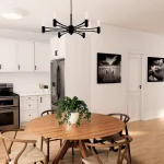Modern open-concept kitchen and dining area at Creekside Trail featuring white cabinetry, subway tile backsplash, stainless steel appliances, and a round wooden dining table with wishbone chairs under a black minimalist chandelier.