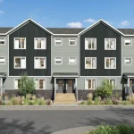 Front streetscape view of modern townhouses at The Grove Townhomes at Wildflower, showcasing multi-toned grey facades, gabled roofs, stone foundations, and pedestrian walkways with native landscaping.