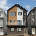 Exterior view of the three-story Ivy detached home model in the Aster community, highlighting a unique half-wood, half-white vertical siding facade with a black framed glass balcony.