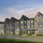 Exterior rendering of Poppy at Rangeview modern townhomes featuring multi-colored facades in blue, grey, and cream with gabled roofs and manicured landscaping under a sunset sky.