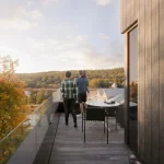 A family enjoying the sunset from a glass-railed balcony of a Calabogie Peaks townhome overlooking the autumn forest and resort lodge.