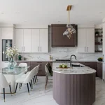 Modern luxury kitchen interior at Kleinburg Hills featuring a curved fluted kitchen island, marble countertops, integrated appliances, and a glass-top dining table.