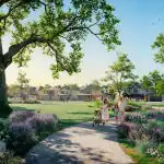 Sunlit park at Creekstone featuring a family with a stroller walking along a path lined with lavender flowers and mature trees, with residential homes in the background.