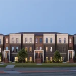 Architectural rendering of Sol Stacked Towns exterior featuring modern multi-level brick and stone facades with landscaped front yards and clean architectural lines under a clear twilight sky.