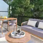 Private outdoor terrace at Sol Stacked Towns featuring a modern patio sofa, a wood dining table with a BBQ grill, and lush greenery providing a serene urban retreat.