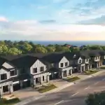 Street-level view of Wasaga Walk townhomes featuring modern farmhouse architecture with white siding, dark gabled roofs, and private garages, set against a backdrop of the lake at sunset.