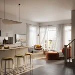 Bright open-concept living room interior at South Banks featuring a kitchen island with bar stools, rust-colored sectional, and large windows with sheer curtains.