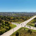 Aerial view of the Bridgelands residential neighborhood showing surrounding greenery, roadways with traffic, and distant city skyline views.