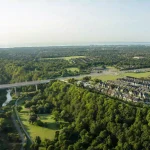 Aerial view of Five Oaks development site surrounded by lush green forests, a river, walking trails, and a bridge in Oakville.