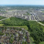 High-angle aerial view showing the expansive Preserve North residential community, surrounding green space, and distant shoreline.