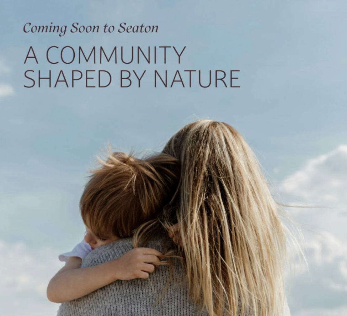 Mother holding a young child against a bright sky, featuring the text "Coming Soon to Seaton - A Community Shaped By Nature" for the Bloom Park development.