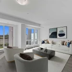 Modern open-concept living room at Countryside Urban Towns featuring white armchairs, a cream sofa, a marble coffee table, and large sliding glass doors.