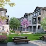 Landscaped community park at Lyric by Lynde Creek with green lawn, picnic tables, benches, flowering trees, and surrounding townhouse buildings.