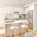 Modern open-concept kitchen interior at Sorella Towns, showing a white kitchen island with bar seating, gold fixtures, marble backsplash, stainless steel appliances, and light hardwood floors.
