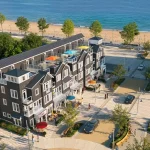 High-angle rendering of coastal townhomes at The Breakers featuring rooftop terraces with umbrellas overlooking a paved plaza, beach, and ocean.
